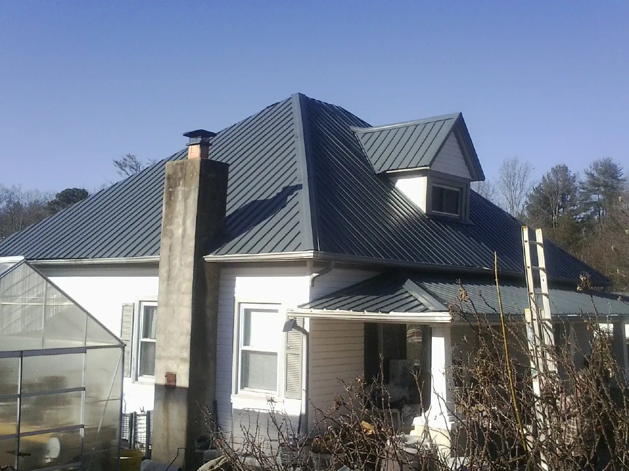 Dark blue standing seam metal roof on a white farmhouse with dormer — Slate & Tile Roof Repair by Roofing Brothers in Underhill