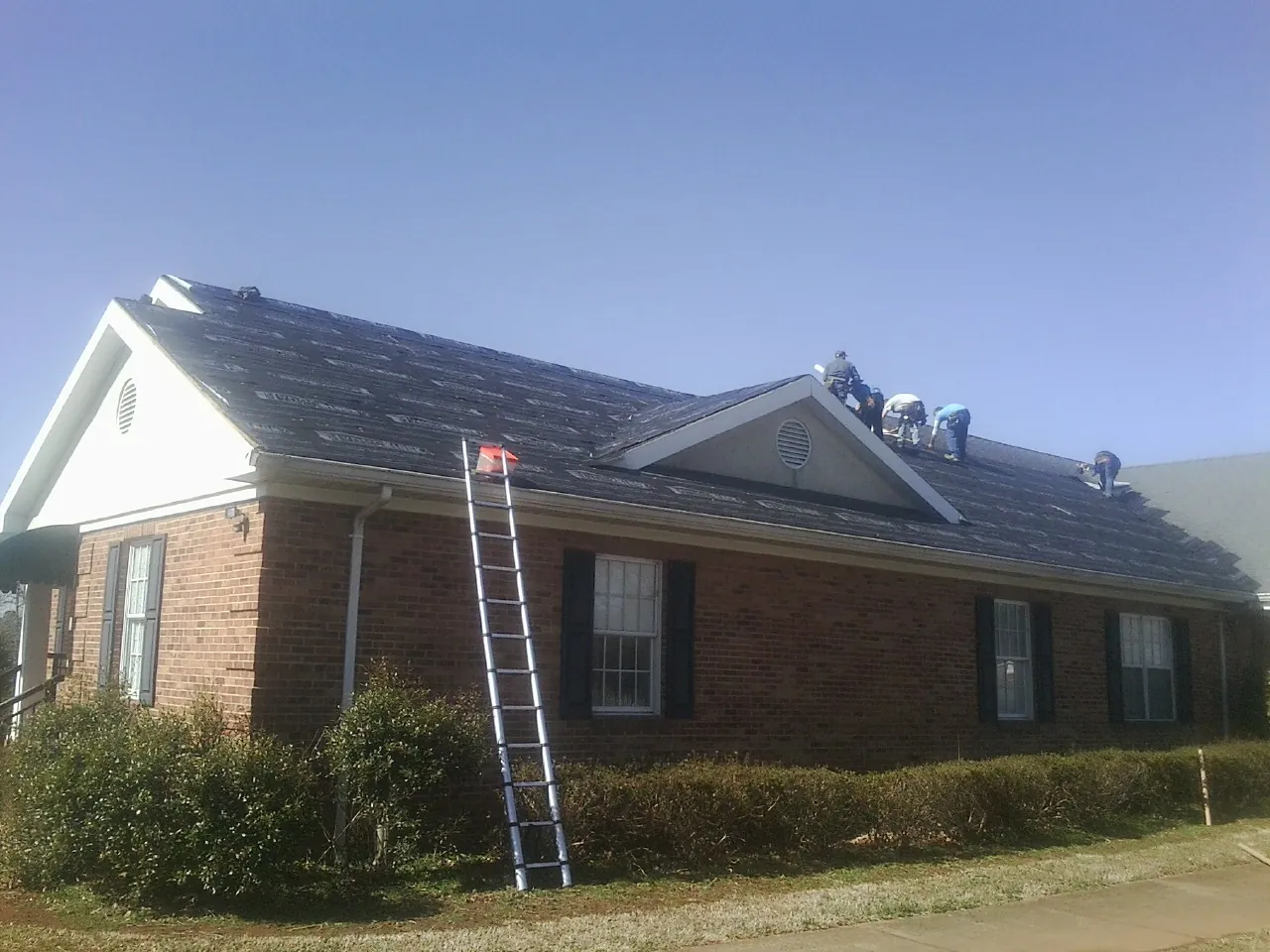 Crew tearing shingles off a brick ranch roof with a ladder set — Emergency Roof Repair work by our crew in Underhill