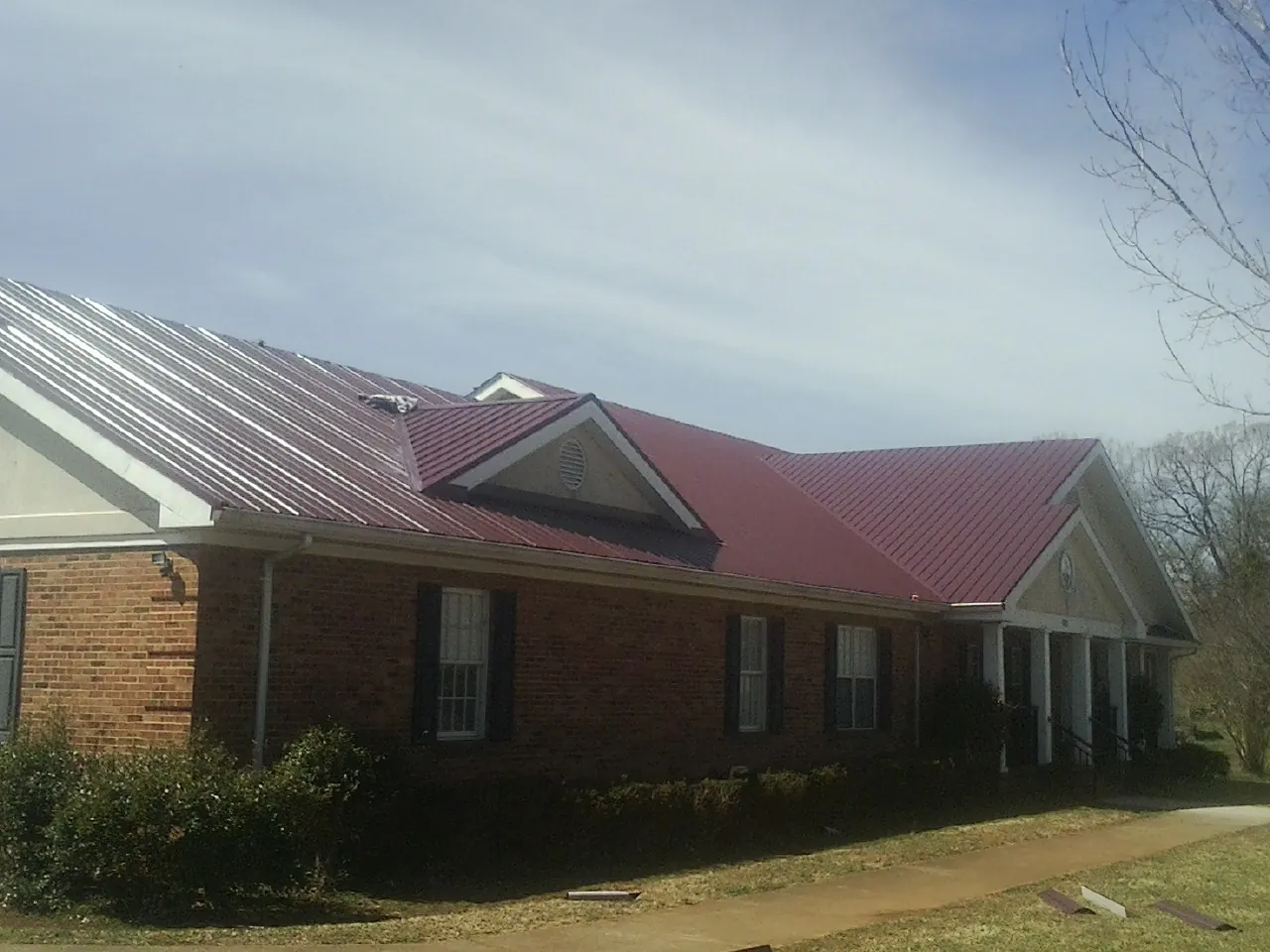 Red metal roof with gabled entries on a long brick building, from a Hail Damage Roof Repair job in Underhill