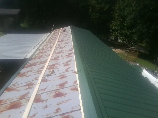 Old rusted panels beside newly installed green metal roofing — Wind Damage Roof Repair by Roofing Brothers in Underhill