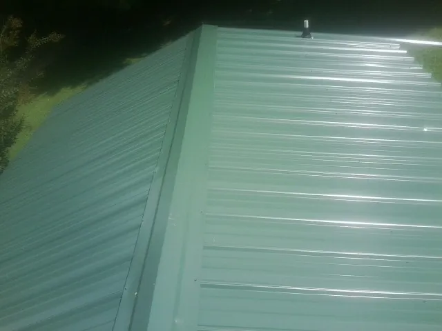New green metal panels meeting at the ridge of a roof — Flat Roof Repair work by our crew in Underhill