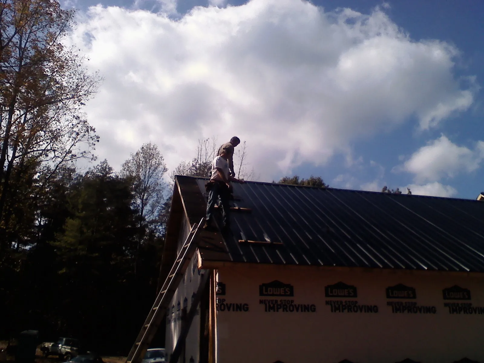 Roofer fastening dark metal panels high against a cloudy sky, from a Roof Inspection job in Underhill