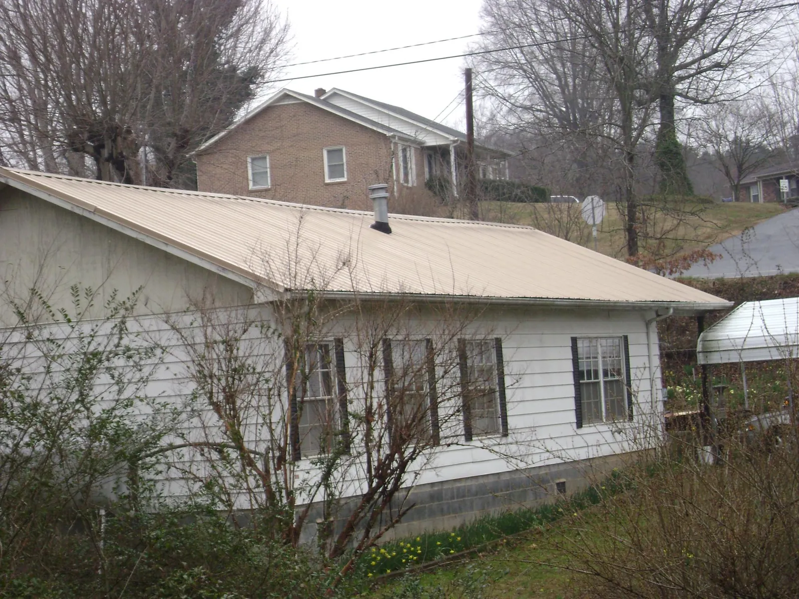 Tan metal roof on a white sided house set into a hillside — Commercial Roofing by Roofing Brothers in Underhill
